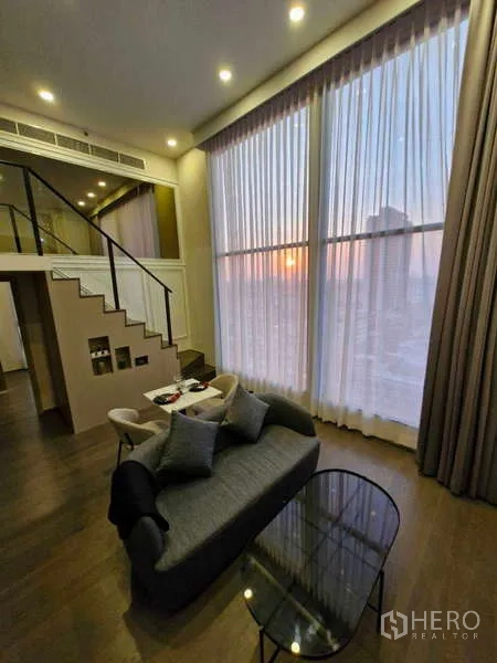 公寓 出售在Ratchathewi, Bangkok - 双层客厅，落地纱帘、沙发与城市日落景观