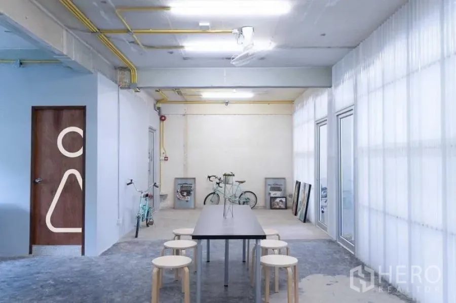 办公空间 出租在Phaya Thai, Bangkok - 开放工作区，两张白色桌子置于工业风天花下，自然光充足的全景窗。