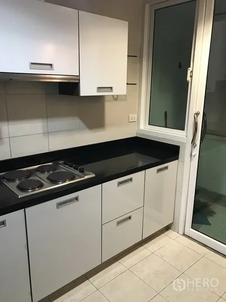 Condominium for rent in Khlong Toei, Bangkok - Compact kitchen with white cabinetry, black countertop, and electric cooktop.