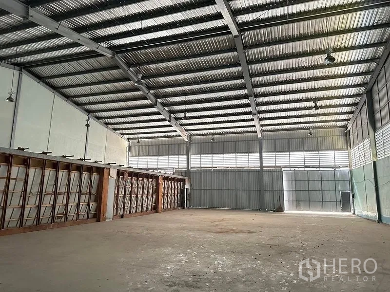 Warehouse for rent in Lam Luk Ka, Pathum Thani - Warehouse interior showing metal roof structure, lighting, and large sliding door.
