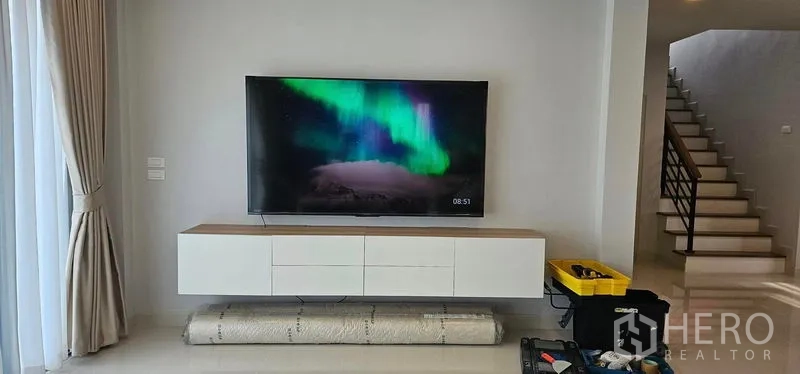 Detached House for rent in Bang Phli, Samut Prakan - Living area TV wall with floating cabinet and staircase to the upper floor in the background.