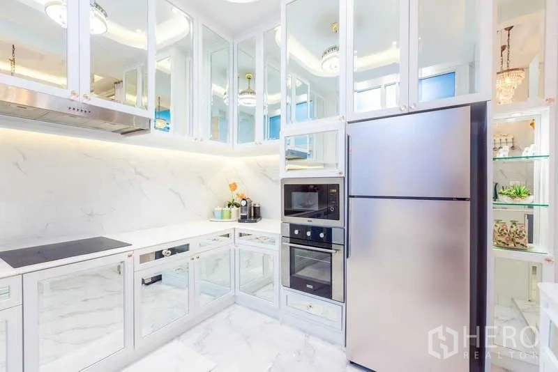 Townhouse for rent in Lat Phrao, Bangkok - White U-shaped kitchen with marble finishes, mirrored cabinets and stainless refrigerator.