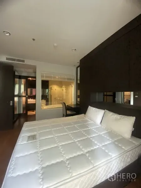 公寓 出租在Pathum Wan, Bangkok - 主卧配大床与隔断书桌，玻璃墙套内卫浴和洗手台。