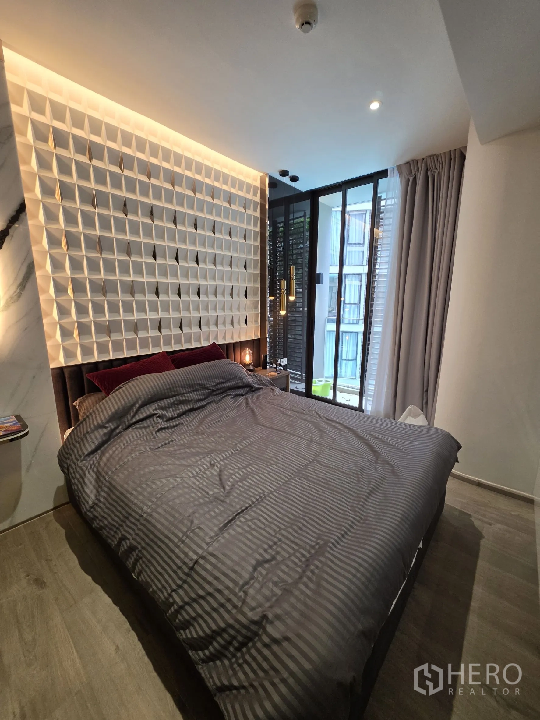 Condominium for rent in Khlong Toei, Bangkok - Bedroom with a queen bed, geometric headboard, and large windows with curtains.