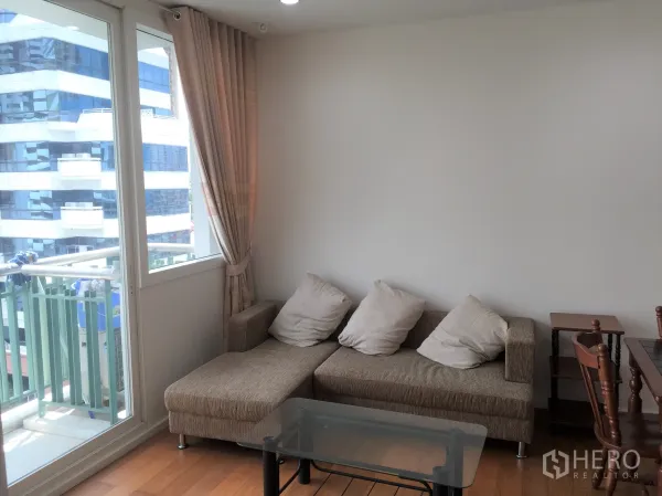 公寓 出租或出售在Watthana, Bangkok - 转角客厅配布艺沙发与玻璃茶几，通往小阳台。