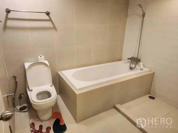 คอนโด ให้เช่าในHuai Khwang, Bangkok - ห้องน้ำสะอาดพร้อมอ่างอาบน้ำแบบฝัง ฝักบัวมือถือ และโถสุขภัณฑ์กระเบื้องสีเบจ
