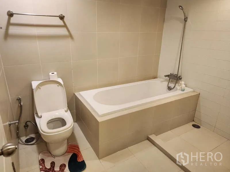 คอนโด ให้เช่าในHuai Khwang, Bangkok - ห้องน้ำสะอาดพร้อมอ่างอาบน้ำแบบฝัง ฝักบัวมือถือ และโถสุขภัณฑ์กระเบื้องสีเบจ