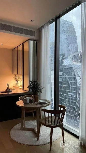 Condominium for rent in Pathum Wan, Bangkok - Cozy dining nook beside floor-to-ceiling window with skyline view next to a compact kitchen.