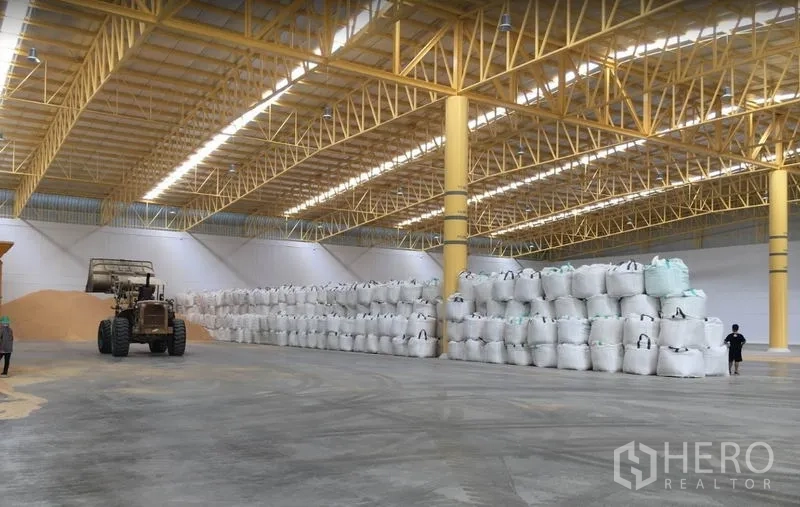 Warehouse for rent in Phra Nakhon Si Ayutthaya - Warehouse storage area with stacked jumbo bags and a loader under a high-clearance roof with yellow columns.