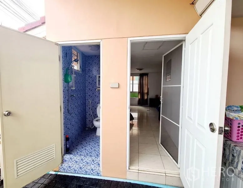 Detached House for rent in Sai Mai, Bangkok - Exterior access to a blue-tiled bathroom beside a utility room with white doors.
