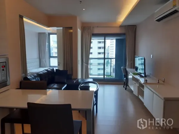 公寓 出租在Watthana, Bangkok - 明亮客厅，皮沙发、电视柜，落地滑门通往城市景观阳台。