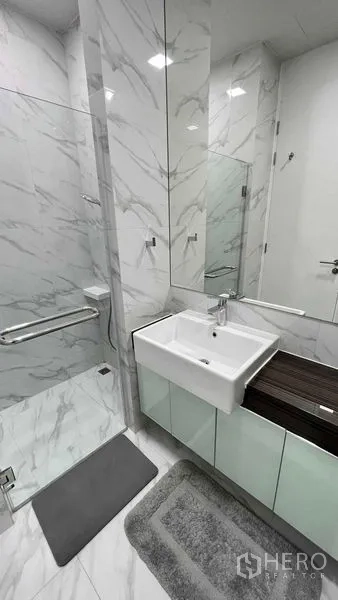 Condominium for rent in Watthana, Bangkok - Glass-enclosed shower beside square basin vanity in a marble-finished bathroom.