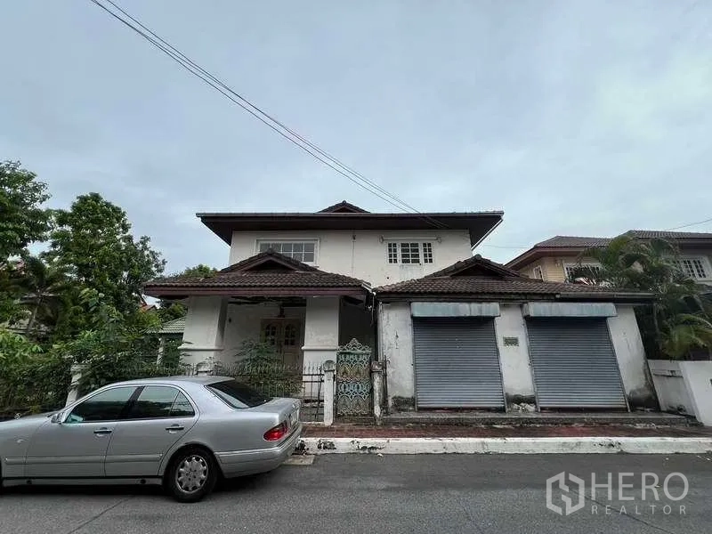 独立式住宅 出售在Phra Khanong, Bangkok - 两层独栋别墅临街外观，瓷瓦屋顶，双卷帘门与小铁门，社区道路安静。
