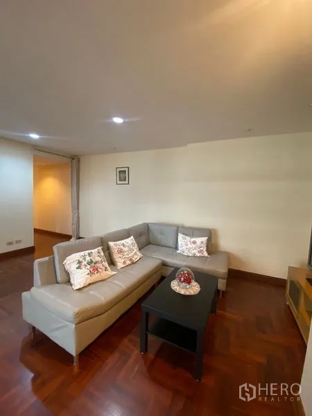 公寓 出租在Pathum Wan, Bangkok - 客厅配L形沙发、茶几与电视柜，拼花木地板。