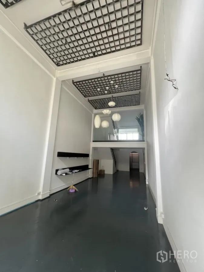 Shophouse for rent or sale in Watthana, Bangkok - Double-height shophouse ground floor with grid ceiling, dark epoxy floor and display shelves.