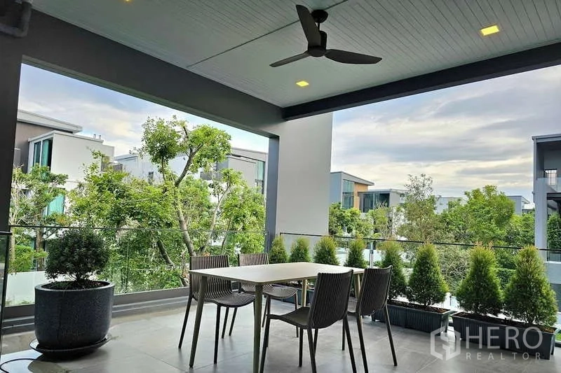 Detached House for rent in Saphan Sung, Bangkok - Covered balcony terrace with ceiling fan, dining set and views over green landscaping.
