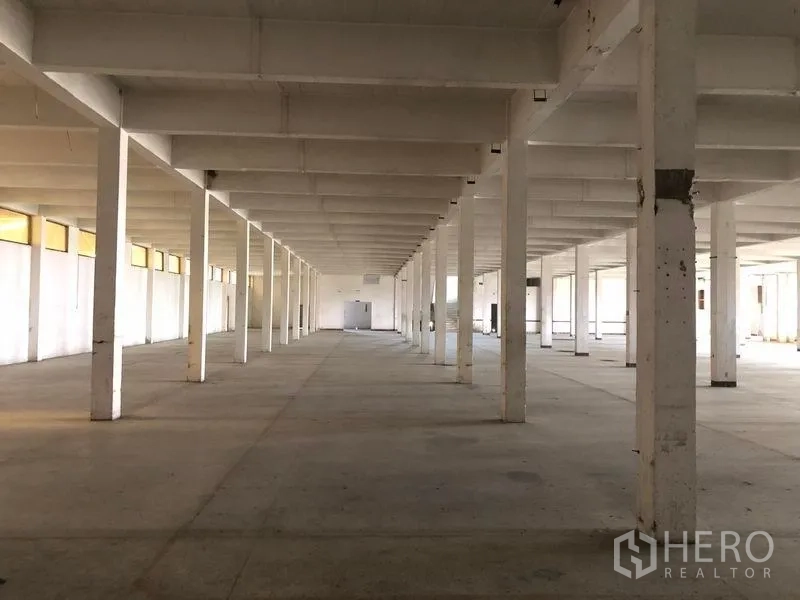 Factory for rent in Bang Phli, Samut Prakan - Open-plan factory floor with white columns, low ceiling grid and natural light from high windows over a concrete slab.
