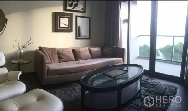 Condominium for rent or sale in Bang Lamung, Chon Buri - Cozy living room with sofa, glass coffee table and sliding doors to a balcony with green views.