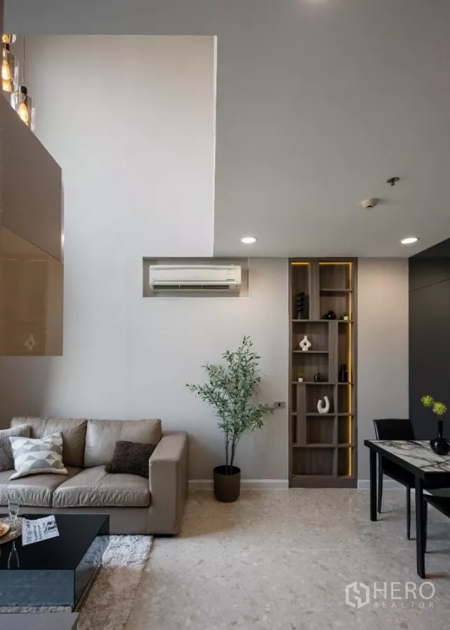 Condominium for rent or sale in Khlong Toei, Bangkok - Open-plan living and dining space with sofa, dining table and display shelves.
