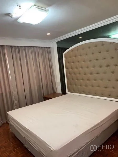 Condominium for sale in Watthana, Bangkok - Master bedroom with a large upholstered headboard, bedside tables, and floor-to-ceiling curtains.