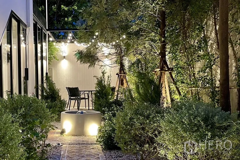 联排别墅 出售在Khlong Toei, Bangkok - 夜晚花园，砖径、树木与露台座椅在灯光下温馨宜人。