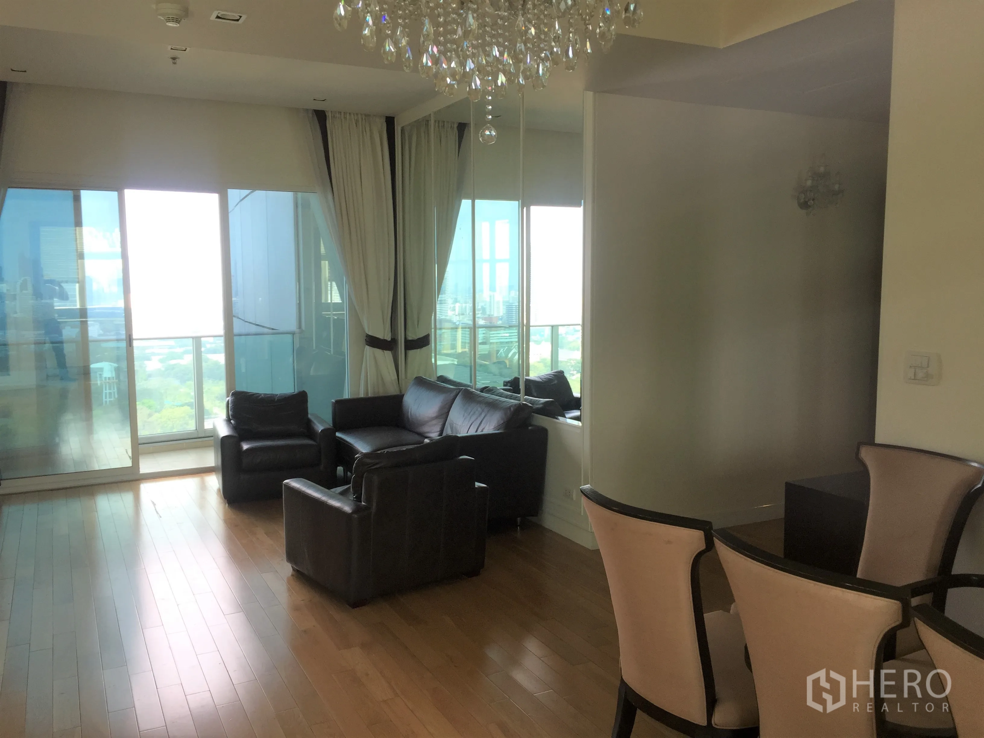 Condominium for rent in Khlong Toei, Bangkok - Living room with leather seating opening to a balcony with wide city skyline views.