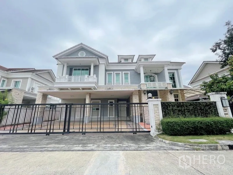 Detached House for rent or sale in Bang Phli, Samut Prakan - Grand exterior of two‑storey detached house with balconies, gated driveway, and manicured hedge.