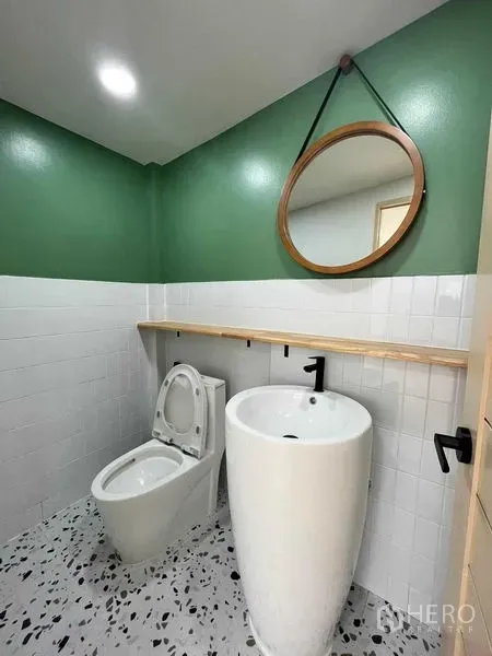 Townhouse for sale in Phra Khanong, Bangkok - Guest bathroom with green accent walls, round mirror, pedestal sink and toilet.