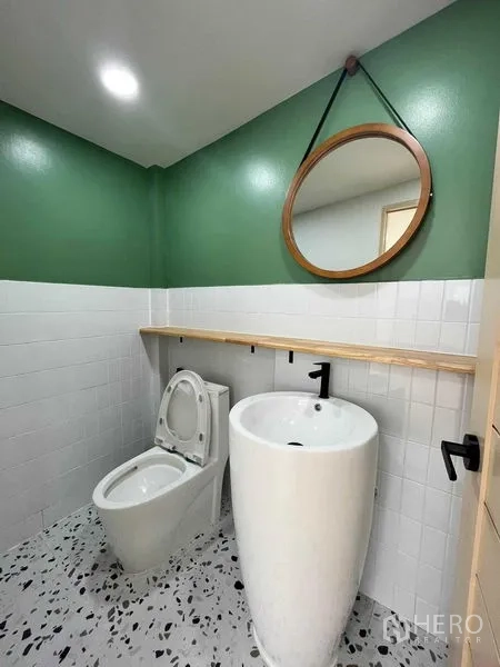 Townhouse for sale in Phra Khanong, Bangkok - Guest bathroom with green accent walls, round mirror, pedestal sink and toilet.