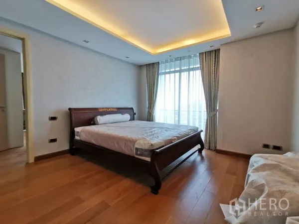 Condominium for rent or sale in Phaya Thai, Bangkok - Primary bedroom with cove lighting, wooden bed frame, and sheer curtains opening to balcony views.