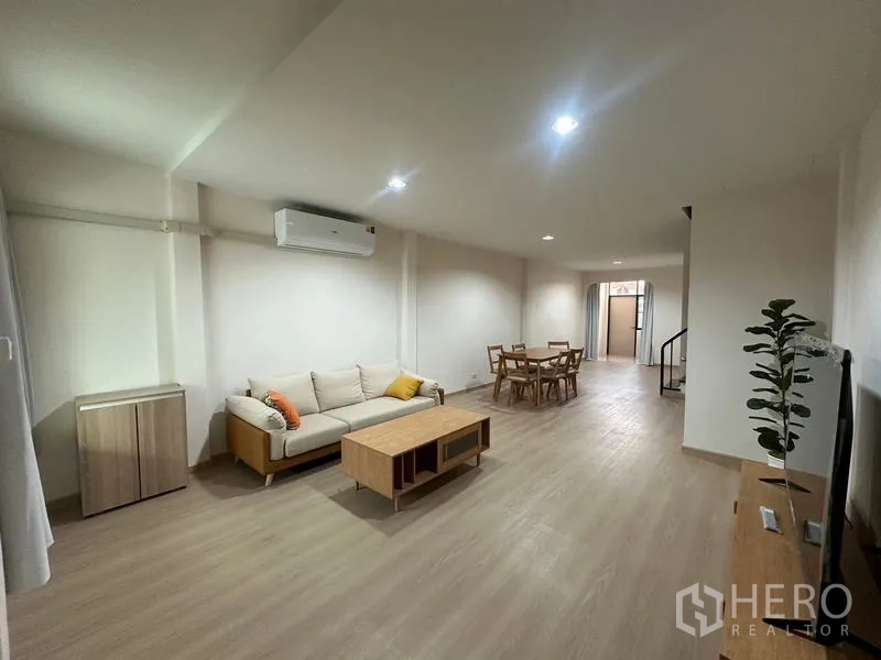 Townhouse for rent or sale in Phra Khanong, Bangkok - Open-plan living and dining area with wood floors, sofa set and recessed lights.