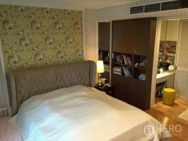 Condominium for rent or sale in Watthana, Bangkok - Master bedroom featuring a tufted headboard, floral wallpaper, built-in storage and access to a vanity area.
