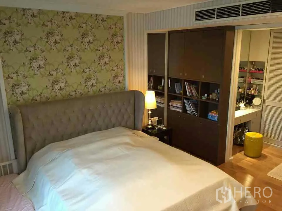 Condominium for rent or sale in Watthana, Bangkok - Master bedroom featuring a tufted headboard, floral wallpaper, built-in storage and access to a vanity area.