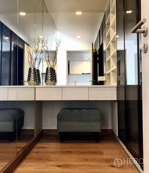 公寓 出租在Watthana, Bangkok - 步入式衣帽间，镜面衣柜与梳妆台及坐墩，木地板与柔和灯光相映。