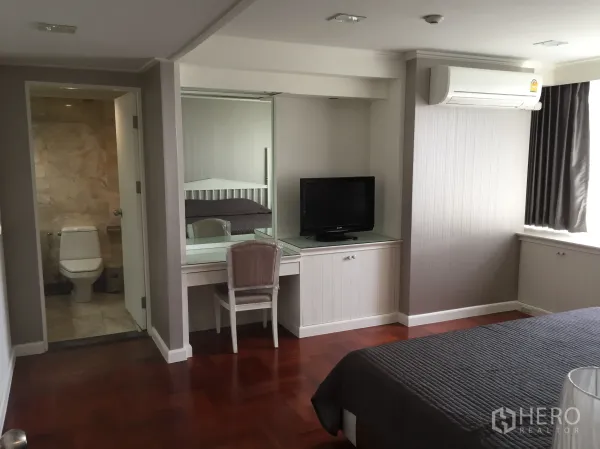 Condominium for rent in Khlong Toei, Bangkok - Master bedroom with ensuite bathroom, air conditioning, TV console, and large curtained window.