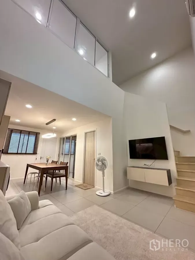 Townhouse for rent in Saphan Sung, Bangkok - Double-height living room with mezzanine glass railing, wall-mounted TV and stairs in a modern townhouse.