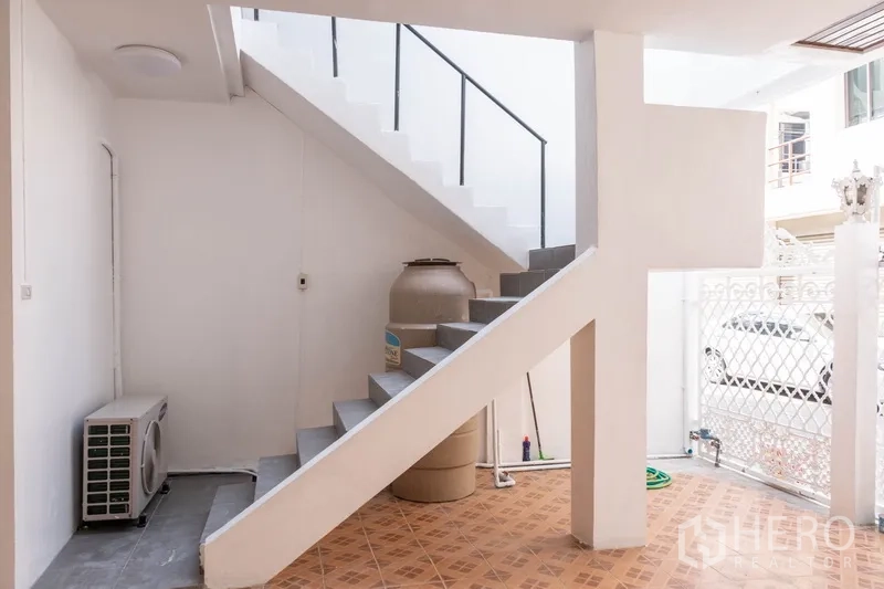 Home Office for rent in Khlong Toei, Bangkok - Ground-floor stairwell and utility area with water tank, AC unit, and white walls.