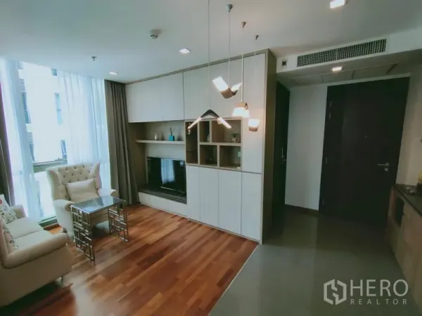公寓 出租在Ratchathewi, Bangkok - 明亮客厅配沙发、电视墙与落地窗及纱帘。