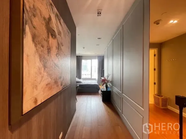 Condominium for rent in Pathum Wan, Bangkok - Warm hallway with wood floors, wall art and paneled storage leading to bedroom.