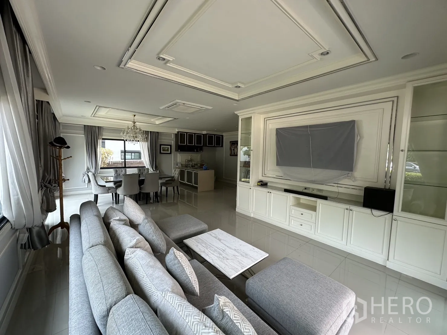 Detached House for rent or sale in Lam Luk Ka, Pathum Thani - Open-plan living and dining area with sofa, chandelier and built-in TV wall.