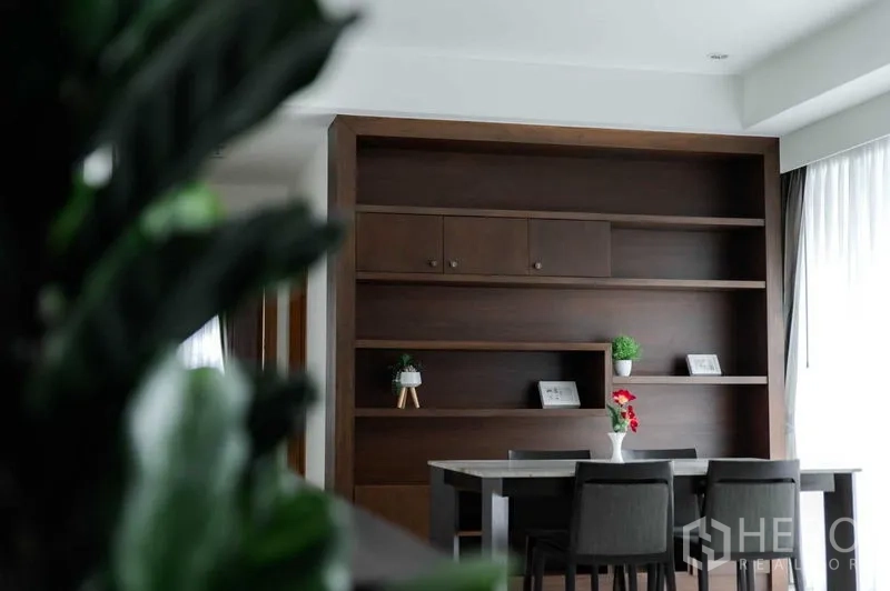 公寓 出租或出售在Bangkok - 餐厅一侧为内置书架与绿植，旁有落地窗。