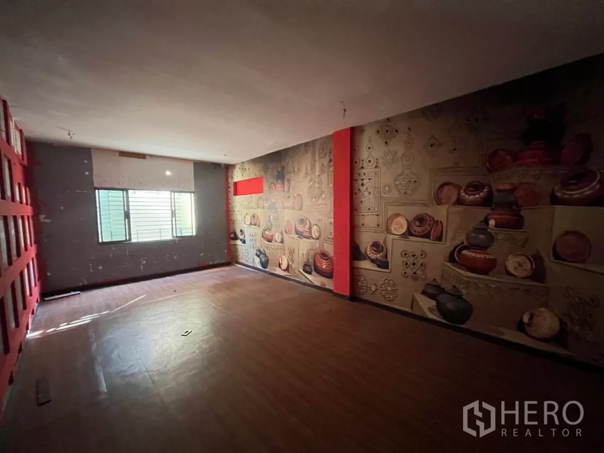 Shophouse for rent in Watthana, Bangkok - Open room with a pottery-themed mural, wood-look floor and natural light from a window.