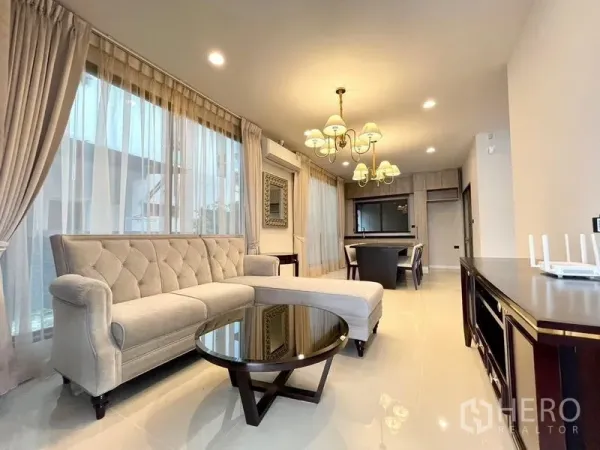 独立式住宅 出售在Bang Kapi, Bangkok - 采光充足的客厅，L形纽扣沙发、圆形茶几、吊灯与落地窗帘。