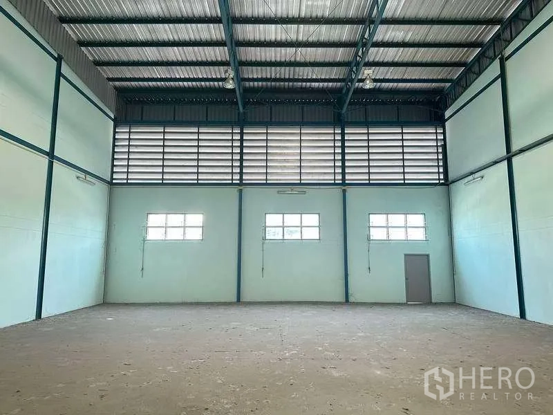 Warehouse for rent in Bang Phli, Samut Prakan - High-ceiling warehouse interior with steel trusses, ventilated louver windows and a side door.