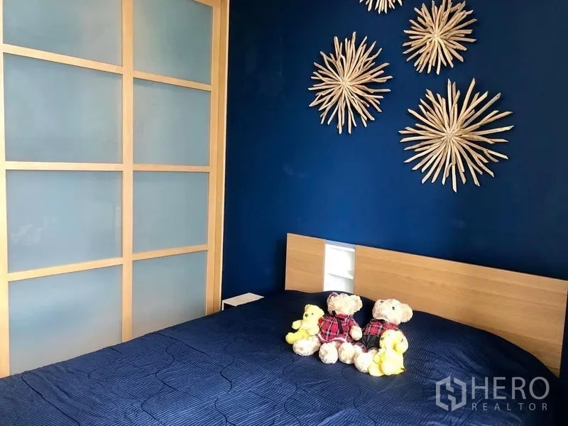 Condominium for rent in Khlong Toei, Bangkok - Cozy bedroom with navy feature wall, wooden bed and sliding frosted-glass wardrobe doors.
