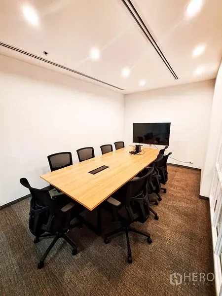 Office Space for rent in Bang Na, Bangkok - Modern meeting room with a long wooden table, black chairs, ceiling lights and a wall‑mounted TV screen.