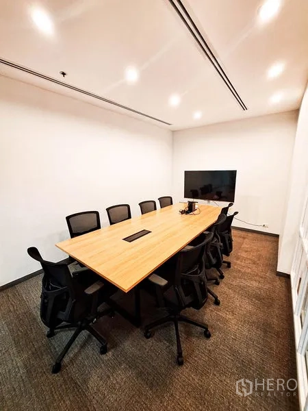 Office Space for rent in Bang Na, Bangkok - Modern meeting room with a long wooden table, black chairs, ceiling lights and a wall‑mounted TV screen.