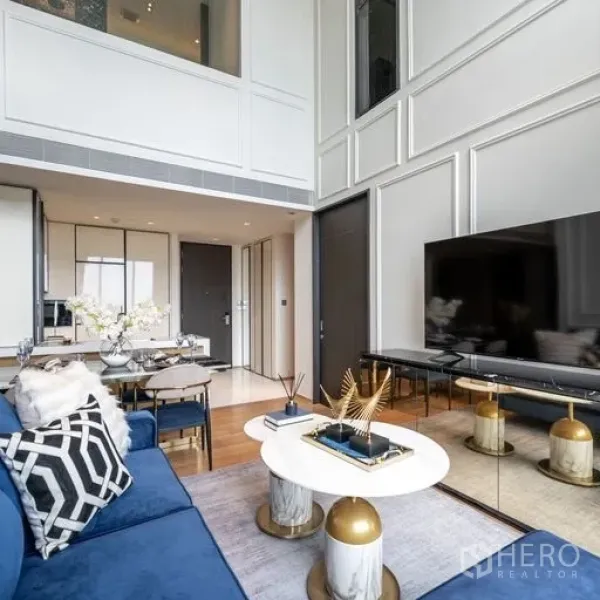公寓 出租在Khlong Toei, Bangkok - 现代客厅，蓝色转角沙发、圆形茶几、大屏电视与通高窗及立体墙板。