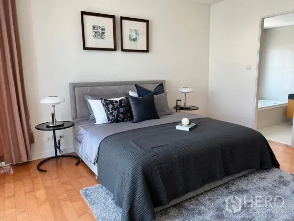 Condominium for rent in Watthana, Bangkok - Master bedroom with upholstered bed, twin bedside lamps, wood flooring, and an ensuite bathroom visible.