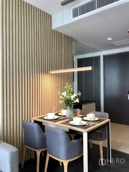公寓 出租在Watthana, Bangkok - 四人用小餐区，灰色餐椅与线性吊灯，旁为木质格栅墙。